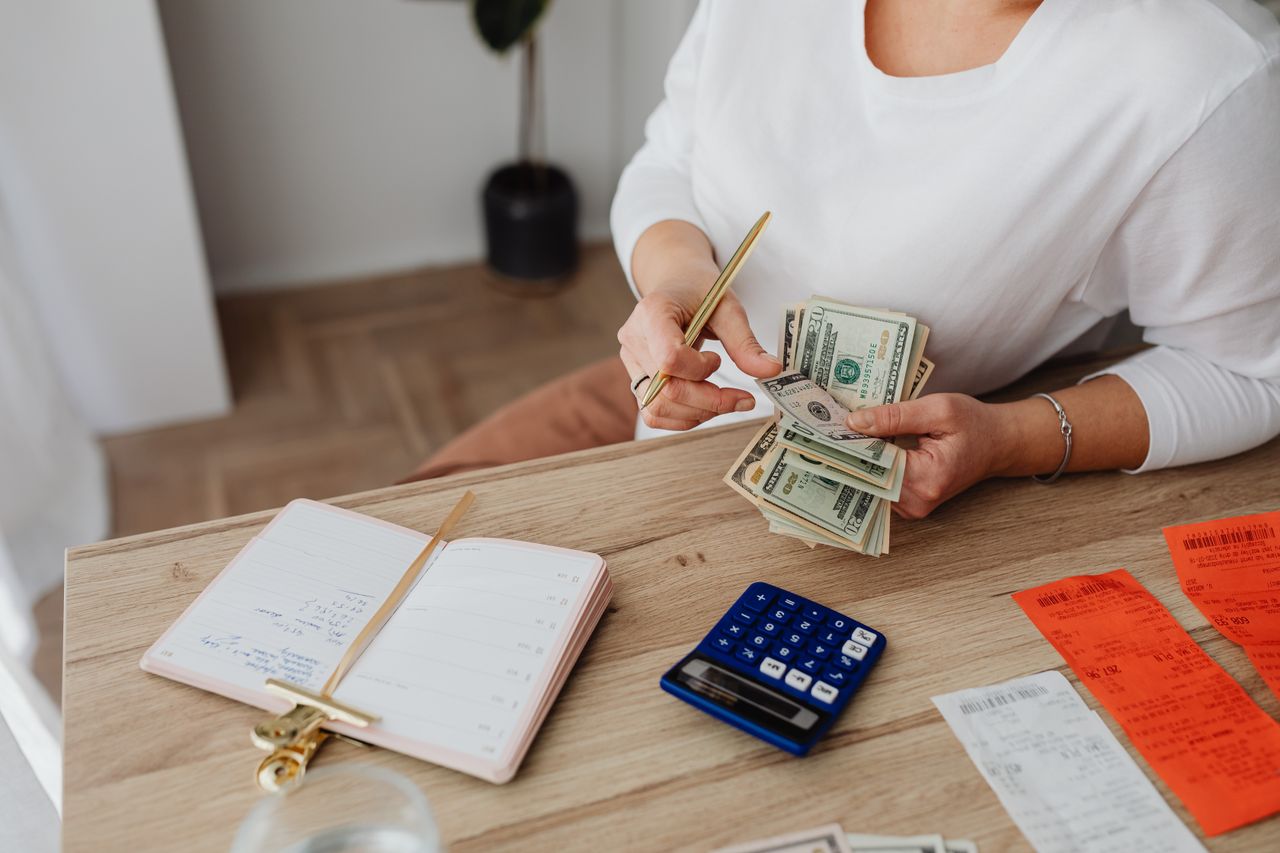 About Woman sorting finances with a calculator, cash, and receipts at a desk.