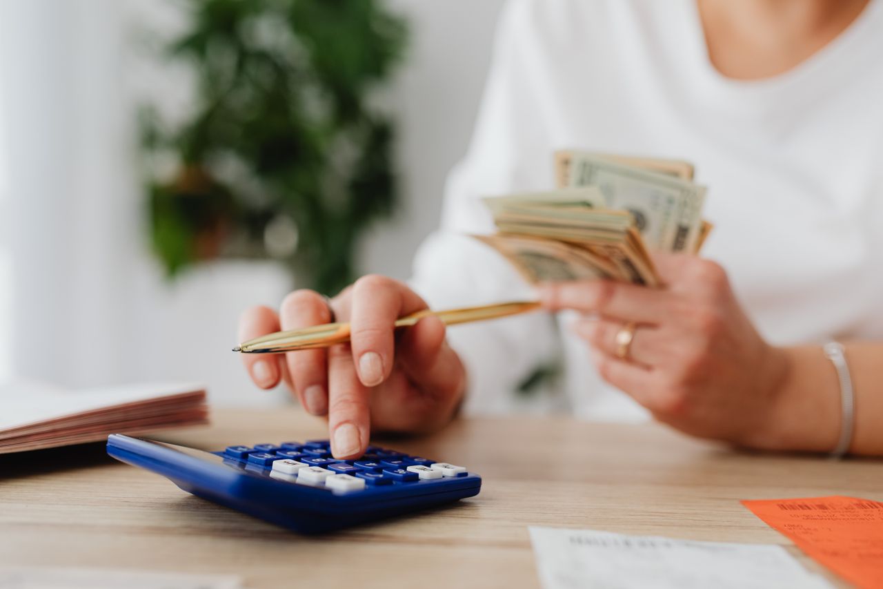 Services A person sits at a desk calculating finances using a calculator and holding cash.