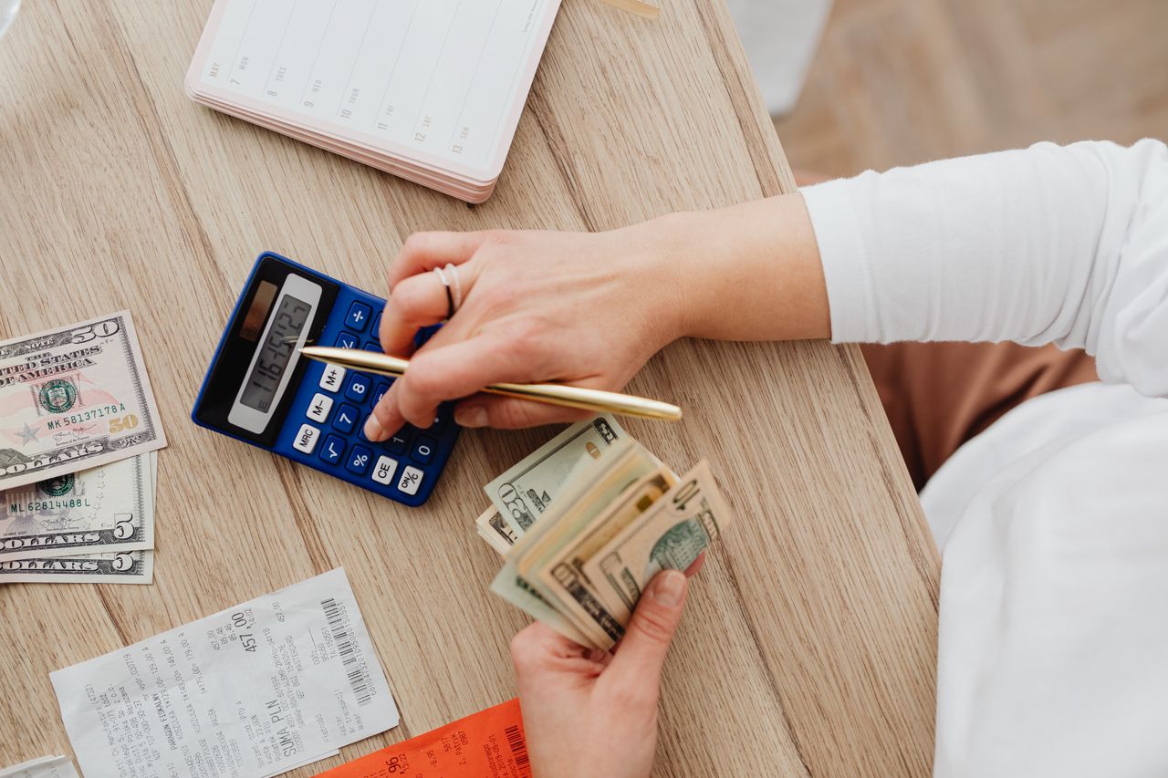 Services Person using a calculator and counting cash on a wooden table with receipts.